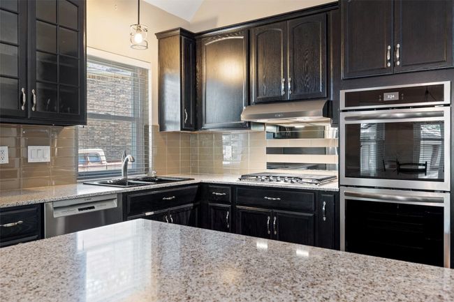 Kitchen with stainless steel appliances, a sink, decorative backsplash, light stone countertops, and dark cabinetry | Image 13