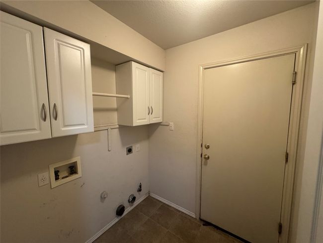 Laundry area featuring cabinet space, hookup for a gas dryer, electric dryer hookup, washer hookup, and dark tile patterned floors | Image 11