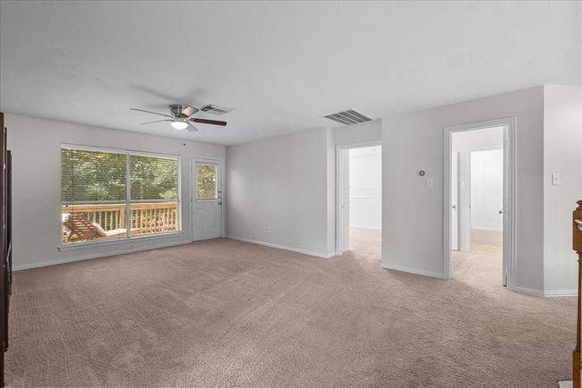This spacious game room features neutral carpeting, a ceiling fan, and a large window with a view of the deck and lake. | Image 24