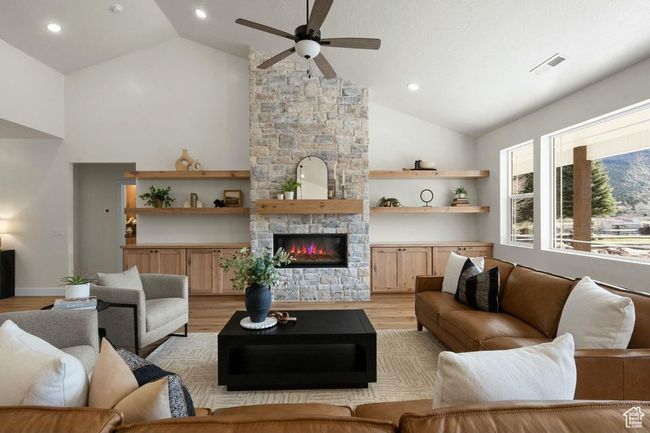 Living area featuring light wood finished floors, visible vents, ceiling fan, a stone fireplace, and high vaulted ceiling | Image 6