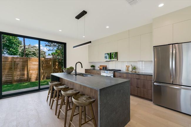 Kitchen with appliances with stainless steel finishes, modern cabinets, dark countertops, a kitchen breakfast bar, and light wood-style flooring | Image 10