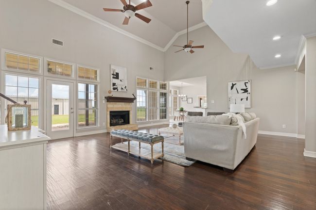 View of living room looking into the breakfast area from the primary suite entrance. Natural light and you can see the workshop in the back as well. Austin stone fireplace, crown molding, two ceiling fans and engineered hardwood floors. | Image 14