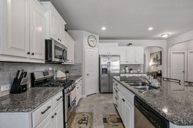 Kitchen featuring stainless steel appliances, a sink, arched walkways, backsplash, and white cabinets | Image 6