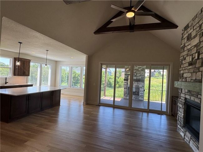 Unfurnished living room featuring a stone fireplace, wood finished floors, plenty of natural light, beam ceiling, and a ceiling fan | Image 8