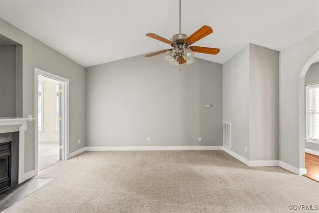 Unfurnished living room featuring carpet flooring, ceiling fan, a fireplace with flush hearth, arched walkways, and lofted ceiling | Image 9