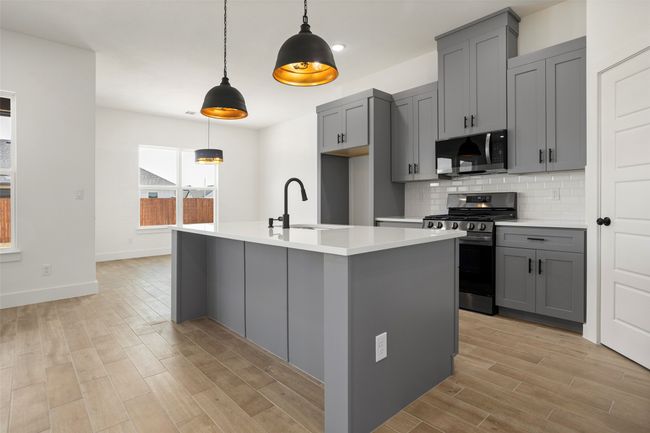 Kitchen featuring appliances with stainless steel finishes, a center island with sink, hanging light fixtures, gray cabinets, and decorative backsplash | Image 8