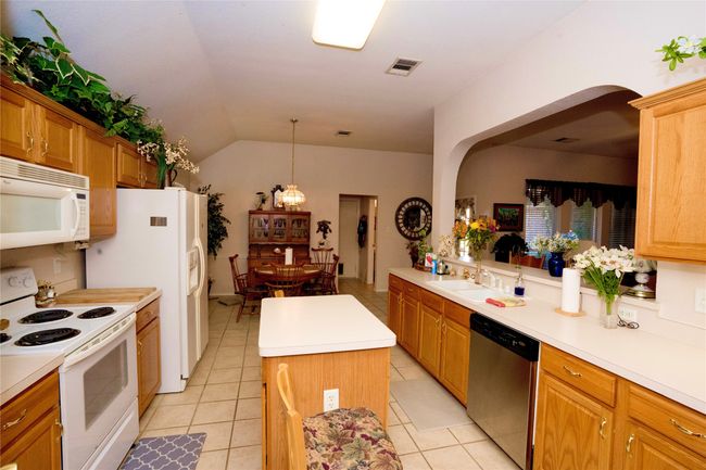 Kitchen with white appliances, a kitchen island, light tile patterned flooring, light countertops, and vaulted ceiling | Image 8