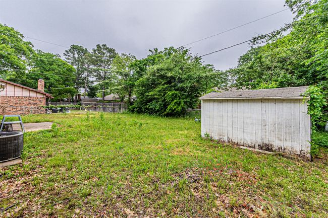 View of yard featuring a storage unit, fence, an outdoor structure, and central air condition unit | Image 36