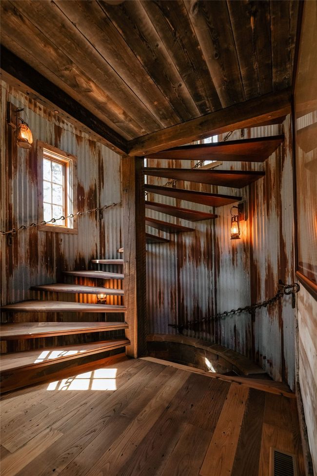 A series of single and double tree horse tack along with a collection of barn lanterns come together as a rustic chandlier illuminating the remarkable walnut spiral staircase spanning all levels in the the silo | Image 26