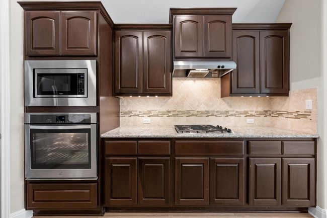 Kitchen featuring stainless steel appliances, dark brown cabinetry, under cabinet range hood, and tasteful backsplash | Image 10