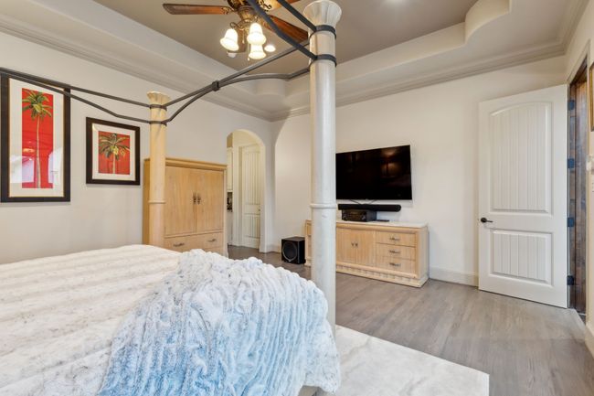 Bedroom with wood finished floors, arched walkways, ornamental molding, and a tray ceiling | Image 12