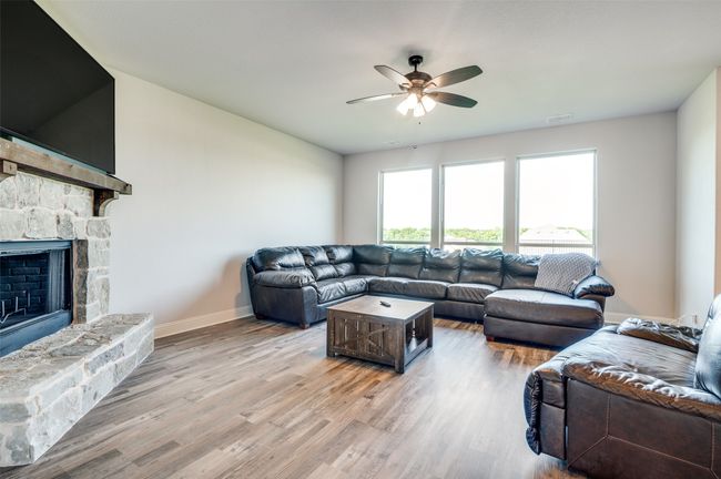 Living room with a ceiling fan, light wood-type flooring, and a stone fireplace | Image 7