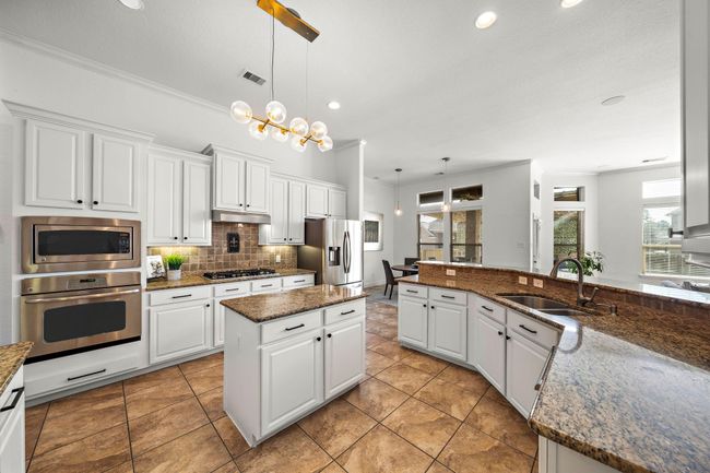 Experience culinary delight in this kitchen, boasting granite countertops and stainless steel appliances. Expansive cabinetry and a central island enhance functionality, while the breakfast bar invites casual dining. The open layout provides seamless flow to the naturally lit breakfast area and living spaces. | Image 18