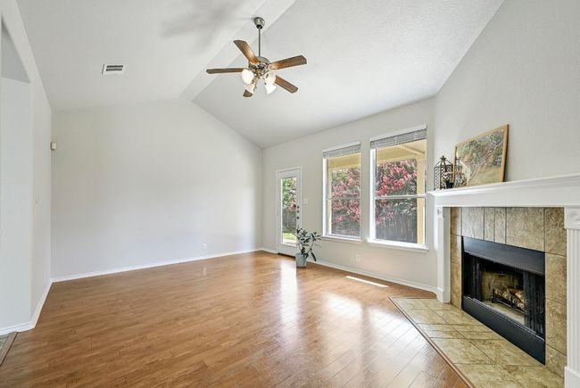 Unfurnished living room featuring a ceiling fan, lofted ceiling, wood finished floors, and a fireplace | Image 4