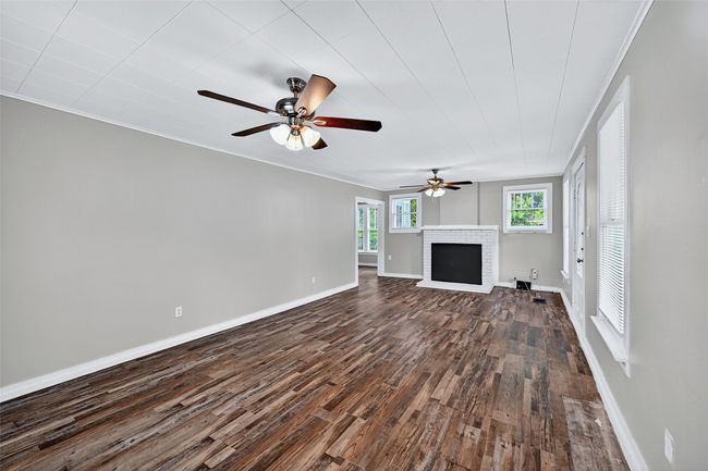 Unfurnished living room with dark wood-style flooring, ornamental molding, a brick fireplace, and a ceiling fan | Image 4