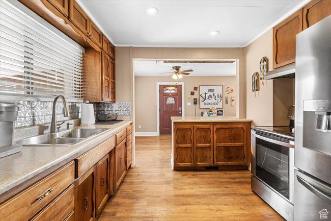 Kitchen with light wood-type flooring, stainless steel appliances, decorative backsplash, a sink, and brown cabinetry | Image 25