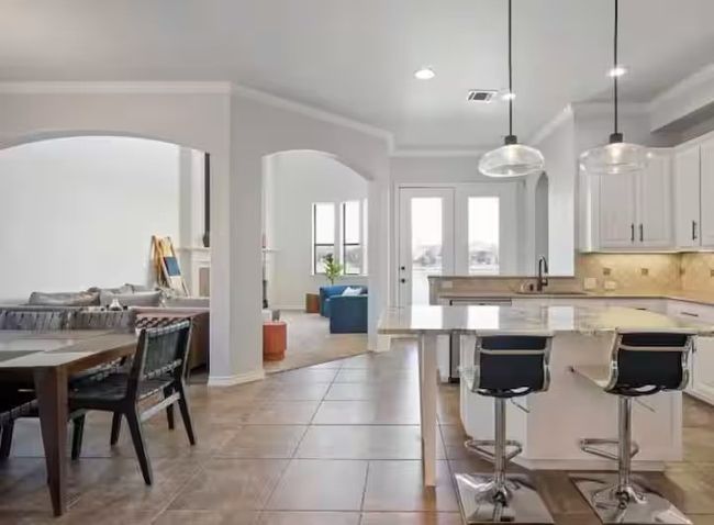 Kitchen featuring arched walkways, ornamental molding, white cabinets, backsplash, and a kitchen island | Image 4