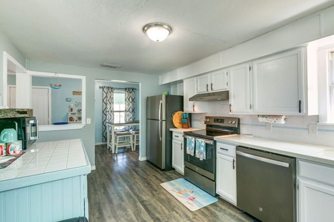 Kitchen featuring under cabinet range hood, dark wood-style floors, visible vents, white cabinets, and appliances with stainless steel finishes | Image 10