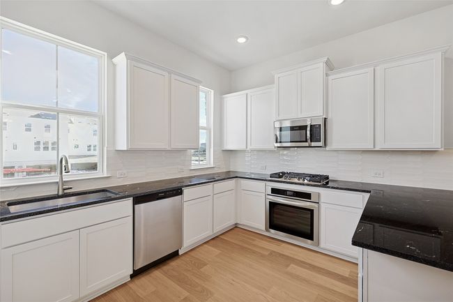 Kitchen with light hardwood / wood-style floors, appliances with stainless steel finishes, white cabinetry, sink, and dark stone countertops | Image 4