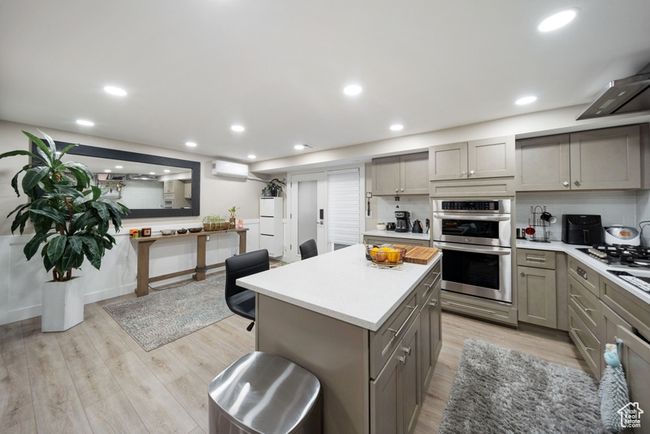 Kitchen featuring gray cabinetry, appliances with stainless steel finishes, a wall mounted air conditioner, light countertops, and light wood-style flooring | Image 21
