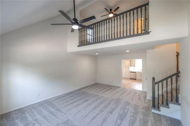 Unfurnished living room with ceiling fan, light carpet, high vaulted ceiling, stairway, and beamed ceiling | Image 5