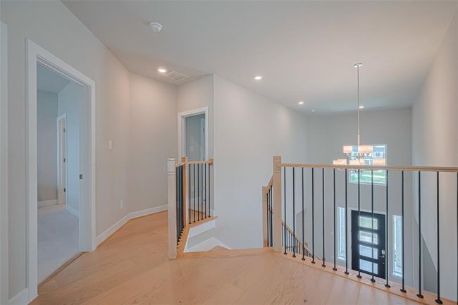 Notice the bright, open second-floor landing with light wood flooring and modern black railing. It features recessed lighting and a hanging chandelier above the entryway. | Image 28