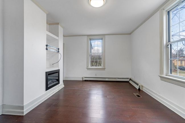 Unfurnished living room featuring wood finished floors, ornamental molding, a glass covered fireplace, baseboard heating, and baseboards | Image 9