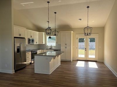 Kitchen featuring decorative light fixtures, appliances with stainless steel finishes, white cabinetry, and a kitchen island | Image 2