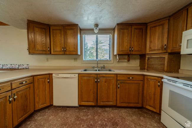 Kitchen with brown cabinets, a sink, white appliances, and light countertops | Image 9