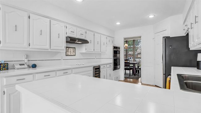 Kitchen featuring under cabinet range hood, wine cooler, white cabinetry, recessed lighting, and decorative backsplash | Image 10