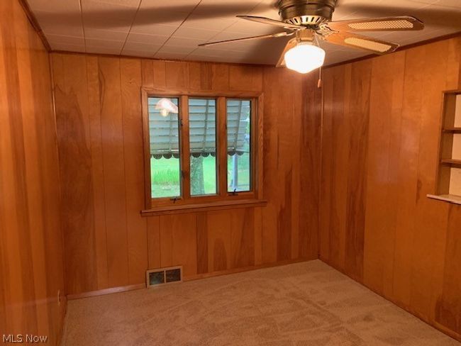 Carpeted empty room featuring wooden walls and ceiling fan | Image 12