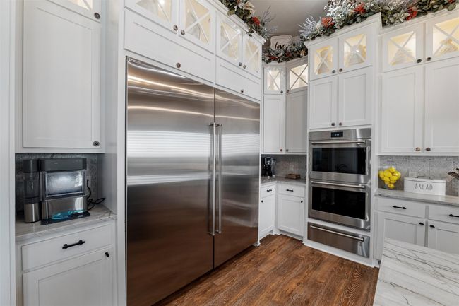 Kitchen with light stone countertops, a warming drawer, stainless steel appliances, white cabinets, and decorative backsplash | Image 21