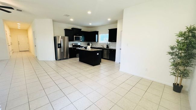 Kitchen with dark cabinetry, a center island, decorative backsplash, appliances with stainless steel finishes, and light tile patterned floors | Image 12