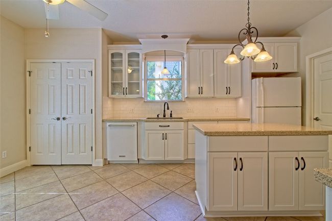 Kitchen featuring freestanding refrigerator, white cabinetry, tasteful backsplash, glass insert cabinets, and hanging light fixtures | Image 13