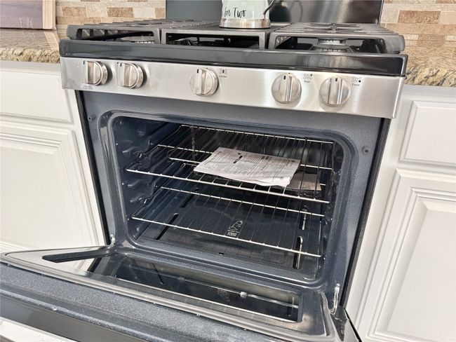 Kitchen view of stainless steel gas stove, white cabinetry, and decorative backsplash | Image 12