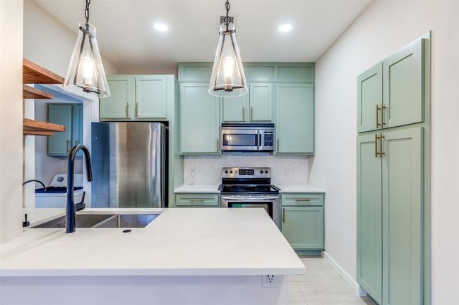 Kitchen featuring stainless steel appliances, green cabinets, decorative backsplash, a peninsula, and decorative light fixtures | Image 8