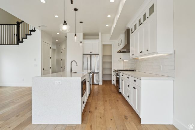 Kitchen with light wood-style flooring, a sink, decorative backsplash, stainless steel appliances, and wall chimney range hood | Image 11