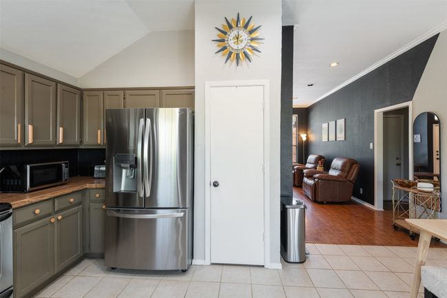 Kitchen with stainless steel appliances, light tile patterned floors, vaulted ceiling, ornamental molding, and open floor plan | Image 7