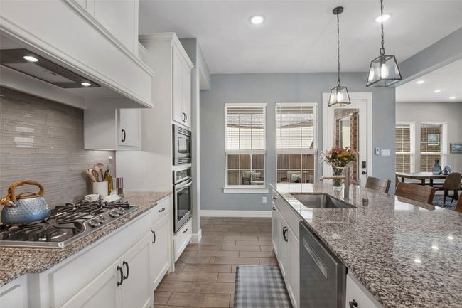Kitchen with stainless steel appliances, a sink, decorative backsplash, custom range hood, and decorative light fixtures | Image 9