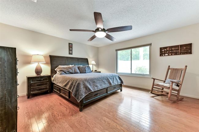 Spacious bedroom with warm wood flooring, featuring a large window for natural light. | Image 8