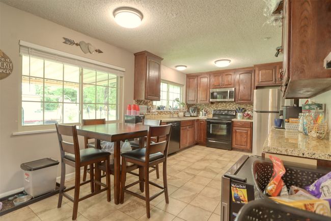 Kitchen featuring stainless steel appliances, tasteful backsplash, a textured ceiling, brown cabinets, and light tile patterned floors | Image 16