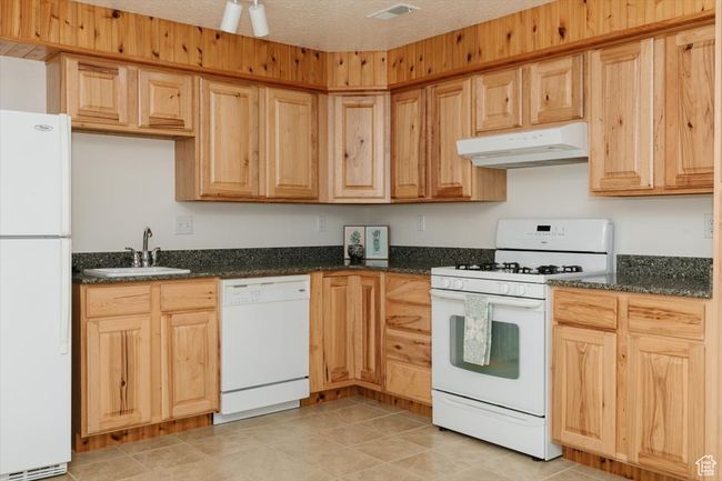 Kitchen featuring white appliances, under cabinet range hood, dark stone counters, and light brown cabinets | Image 50