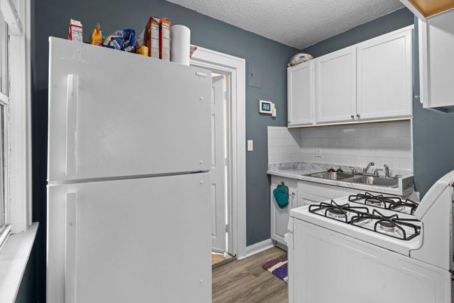 The kitchen features luxury plank flooring, white cabinetry, and a gas stove, with a window offering views of the side yard. | Image 4