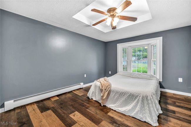 Bedroom featuring a baseboard heating unit, wood floors, ceiling fan, and a textured ceiling | Image 21