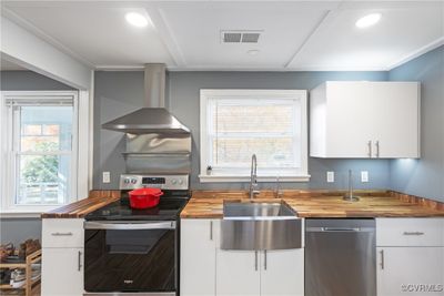 Kitchen featuring white cabinetry, stainless steel appliances, wall chimney range hood, and butcher block countertops | Image 3