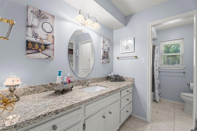 This bathroom features a spacious granite countertop with an oval mirror, light gray walls, and tasteful decor. It includes ample cabinet storage, elegant lighting, and a separate shower area with a window for natural light. | Image 18