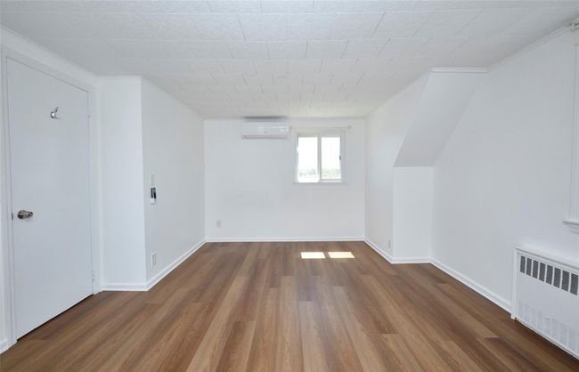 Bedroom featuring radiator heating unit, a wall mounted air conditioner, wood finished floors, and baseboards | Image 19