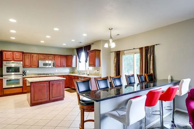 Kitchen with a breakfast bar area, a center island, light tile patterned floors, stainless steel appliances, and recessed lighting | Image 5