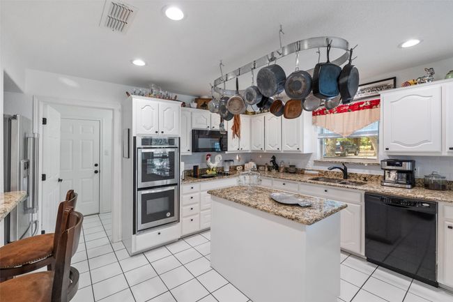 Kitchen featuring white cabinetry, visible vents, black appliances, light tile patterned flooring, and a sink | Image 8