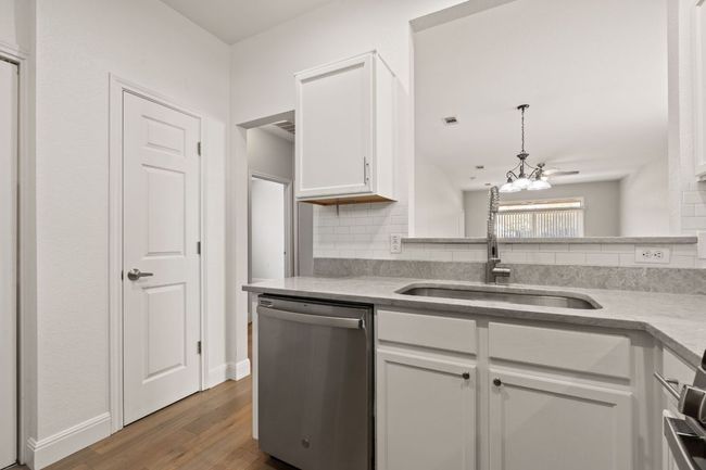 Kitchen featuring tasteful backsplash, stainless steel dishwasher, a sink, white cabinets, and wood finished floors | Image 9